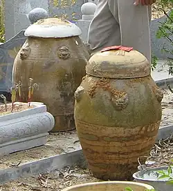 Two large, rounded urns with ochre and faded green decorative elements. They are fitted with rounded lids and come to just above knee height.