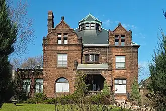 Asymmetrical, two-and-a-half-story stone house with an ornate dormer at the roof peak