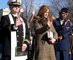 Klingenschmitt (left), a white woman in civilian clothes, and a black woman in an Air Force captain's uniform, standing abreast outdoors, with their eyes closed and right palms raised forwards