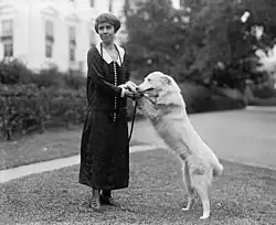 Grace holding the front paws of a white collie as it stands on its hind legs reaching her waist