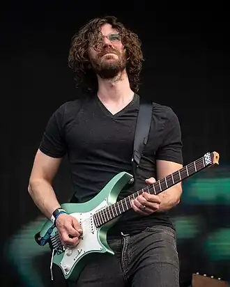 Randy McStine wearing a black t-shirt an black jeans, playing a green and white electric guitar onstage while looking straight ahead