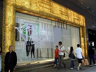 Glass shopfront with textured, illuminated border, from which a sign saying "Joyce" hangs.