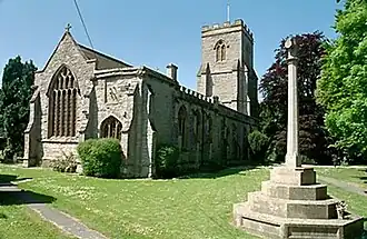 Stone church with arched window and square tower, with a stepped churchyard cross to the right