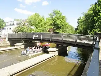 Steel bridge over water against a blue sky with green trees