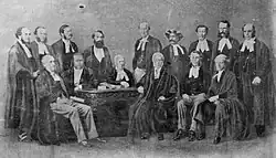The High Court at Calcutta in 1865; standing (from left to right): Arthur George McPhearson, Elphinstone Jackson, Frederick Augusta Bernard Grover, John Budd Phear, Charles Steer, Sumboo Nath Pundit, Francis Baring Kemp, George Campbell, and John Paxton Norman; sitting (from left to right): Charles Binny Trevor, Henry Vincent Bayley, Walter Scott Seton-Kari, Sir Barnes Peacock, Walter Morgan, and George Loch