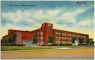 A hand-tinted postcard of three-story, red brick school building.