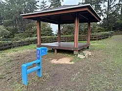 A simple wooden pavilion with a simplified blue pony metal sculpture marking the Olle Trail in front of it