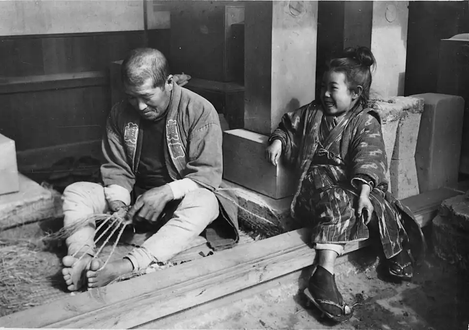 Zori were traditionally made at home, as were waraji. Note twine warp, held between hands and toes, and loose-fiber weft, to his right.