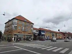 An urban block of modern brick buildings in Copenhagen, including a library and supermarket, with a pedestrian crossing in the foreground.
