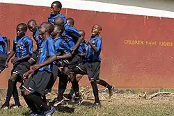 A picture of Ugandese children in football uniforms. On the wall behind them is engraved, "Children have rights".
