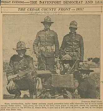 Five Iowa National Guardsmen in uniform posing by a machine gun