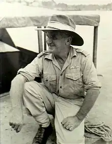 Informal portrait of Pentland in light-coloured military uniform with wide-brimmed hat, crouching on one knee