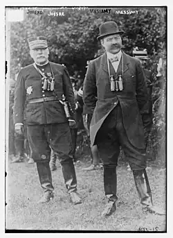 The general in simple uniform, the civilian in jacket and bowler hat, both wearing binoculars and boots.
