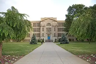 Front shot of John Adams High School, a multistory beige building with trees on either side