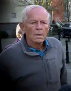 An old man with thin white hair and a combover making a displeased facial expression.