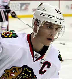 Jonathan Toews in a white away Blackhawks jersey and wearing a white helmet with a clear shield covering his eyes.