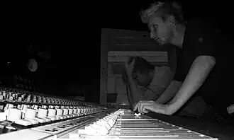 black-and-white image of Jukka Backlund leaning over audio control board, next to a seated man
