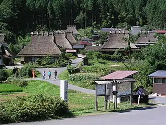 Wooden houses with thatched roofs in a mountain setting.