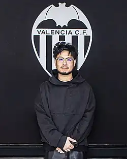 A photograph of Lim in a black hoodie and a Valencia CF logo background