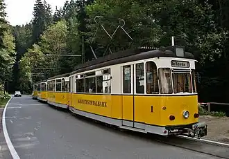 Three coupled single car trams on a road through a forest