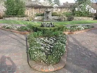 Photograph of a formal garden at the Luther Burbank House and Gardens, featuring brick walkways and planterboxes, a small lawn, a fountain and pool, low stone walls, and wooden trellises.