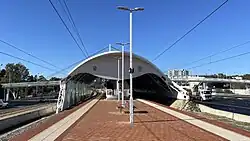 Train station island platform with a curved metal shelter covering the platform and tracks