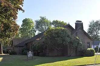 Brown wood building with multiple gables and a large stone chimney, surrounded by trees