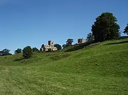 Grassy ground sloping upwards, with a stone-built church in the distance.