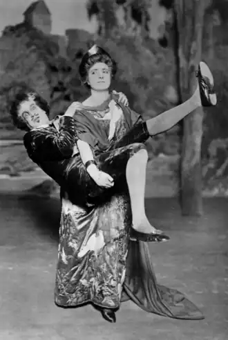 White woman in Victorian "aesthetic" costume carrying a white man, who looks comically terrified