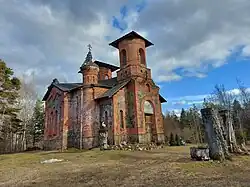 a colour photograph of the beautiful "Maaritsa Church of the Transfiguration of Our Lord" it is a building made of a mix of red brick and dark stone. it had 3 short spires with a cross atop the shortest of them.