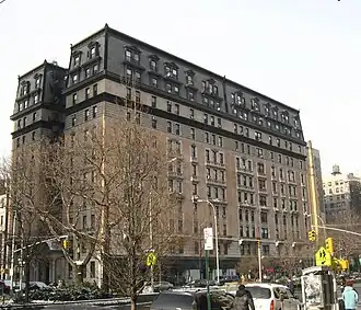 View of the Manhasset from the intersection of Broadway and 108th Street. The facade is largely made of salmon brick, except at the base, where it is made of stone. The top of the building contains windows within a black mansard roof.