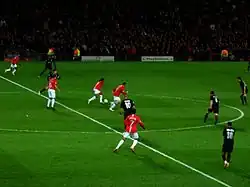 A wide shot of a football match with Manchester United in red in possession against Lyon in black.