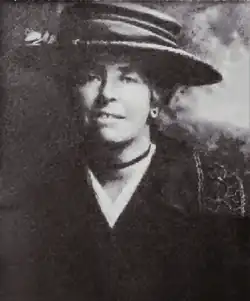 Cunnington in semi-formal dress as a young woman, wearing a wide-brimmed hat, a cardigan and a white blouse