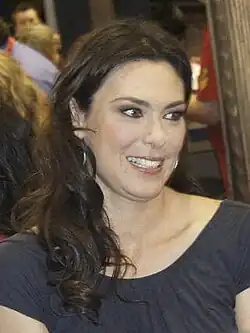 A Caucasian woman with brunette hair wears a dark grey blouse.