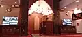 Qibla of Masjid Mydin, with mihrab and minbar visible as well as digital prayer clock and monitor screens.