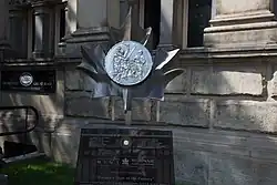silver metal sculpture shaped like a coin situated outside a building