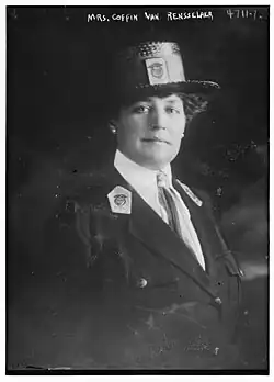 A white woman wearing a dark boater hat and a uniform-style jacket with lapel insignia