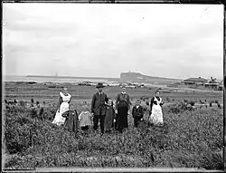 Mrs. and Mr. A. Graham's family standing at Stockton with breakwater, masts of shipwreck, and Nobby's Head in background.