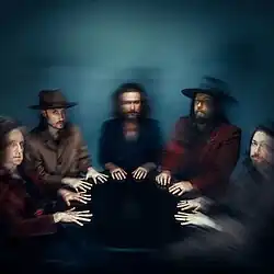 A blurry image of the members of My Morning Jacket with their hands on a black table.