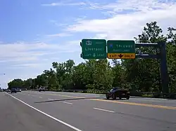 Overhead sign on a four-lane road with a New York state route marker instead of the pentagonal county shield