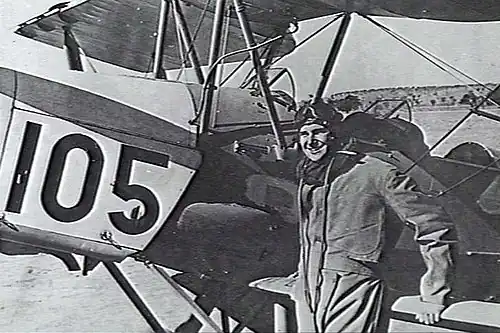 Pilot in flying gear next to biplane