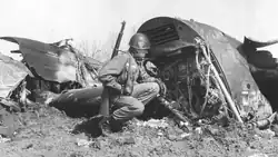 A soldier squatting down next to a large piece of aircraft wreckage