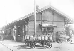 Norwalk, CA depot with deep eaves, loading docks and storefronts. A wagon, fully laden with milk cans is in front.