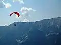 Note kite's wing and many kite lines held by human operator; operator moves by gravity (paraglider kite system)