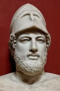 Bust of white marble shoulders up over a red background wearing a tall helmet with a large curly beard