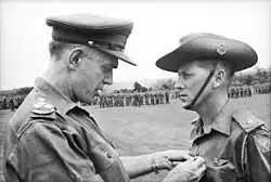 Black and white photograph of Brigadier (Oliver) David Jackson pinning the Military Cross on Harry Smith in military uniform, 1967