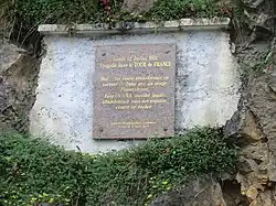 Memorial plaque reading the translated words "Monday July 12, 1971, tragedy in the Tour de France. On this road transformed into a torrent of mud by an apocalypse storm, Luis Ocaña, a yellow jersey, gave up all his hopes against this rock."