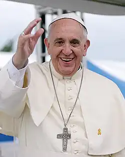 Headshot of Pope Francis wearing papal regalia. He is clean-shaven and bald. His dress consists of a white cassock with matching pellegrina and with white-fringed fascia, silver pectoral cross, and white zucchetto.