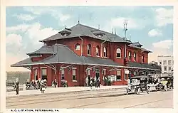 A postcard showing a two-story brick train station on an urban street
