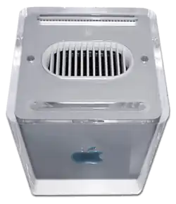 A silver cubic computer with rounded edges, viewed from above, with a large cooling vent and optical drive slot visible on the top.
